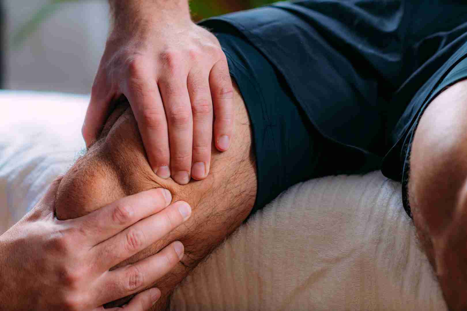 A close-up photo of a person receiving a knee massage. A pair of hands is seen applying pressure and massaging the knee area, possibly indicating physiotherapy or relief for knee pain, as one might experience at Austin Manual Therapy Associates. The person being massaged is wearing shorts.